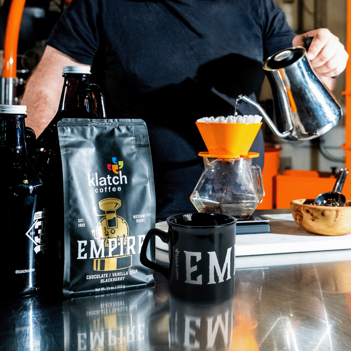 Person making coffee with Klatch Coffee Empire bag and Empire mug on a counter.