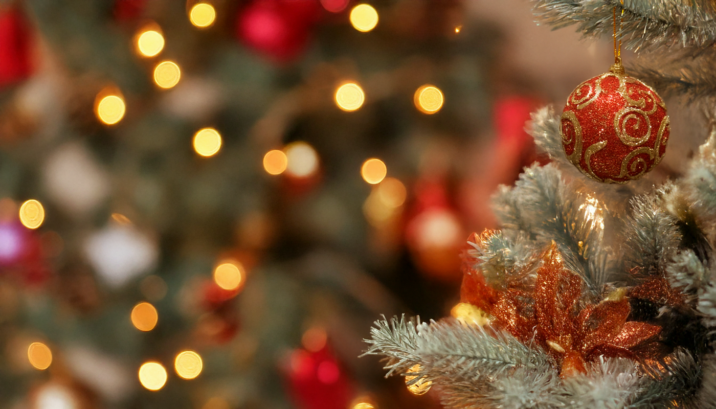 Red ornament on a Christmas tree with bokeh holiday lights in the background.