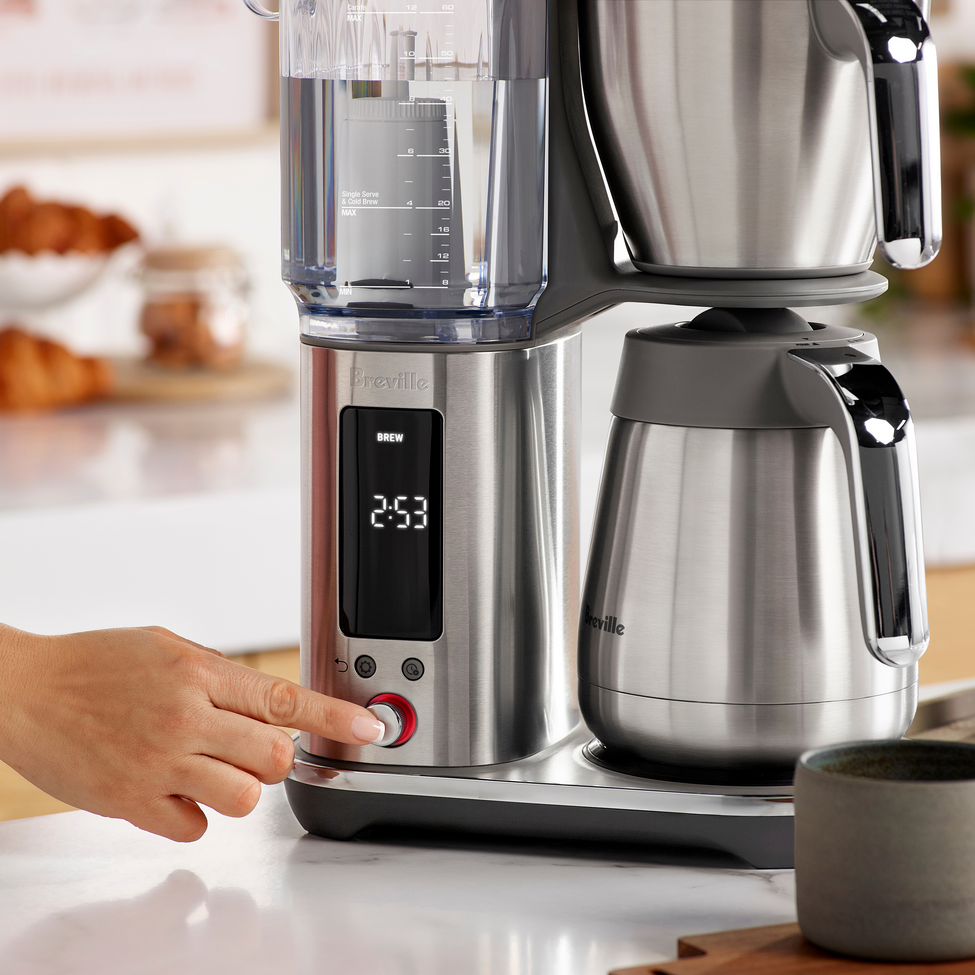 Stainless steel coffee maker on a kitchen counter with a hand adjusting settings.
