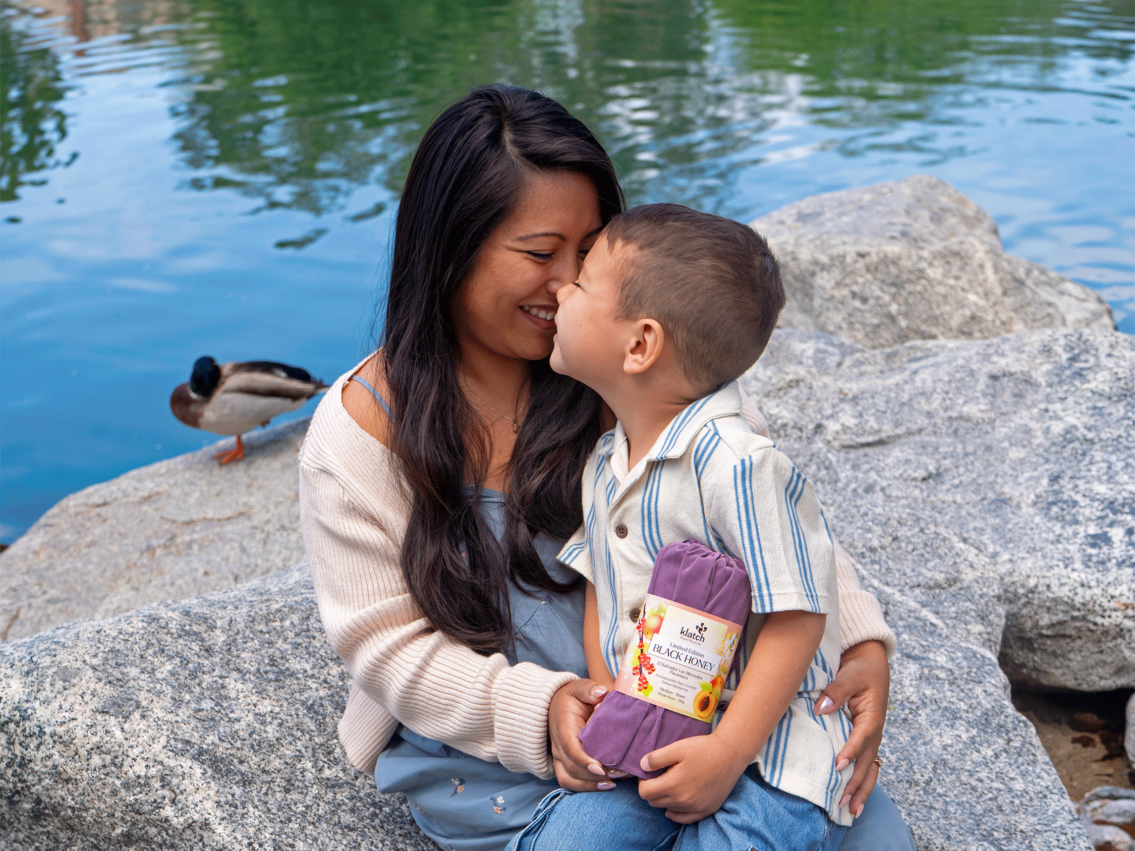Mother kissing her son’s head by a lake while holding Klatch Coffee’s Black Honey Pearl Reserve Coffee.