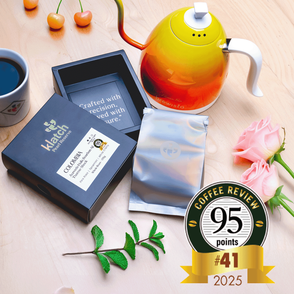 Pearl Box with a kettle, white cherries, spearmint, pink roses, and a coffee review badge on a wooden table.