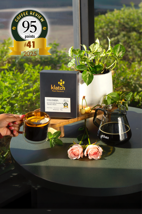 Pearl Box with a kettle, white cherries, spearmint, pink roses, and a coffee review badge on a wooden table.