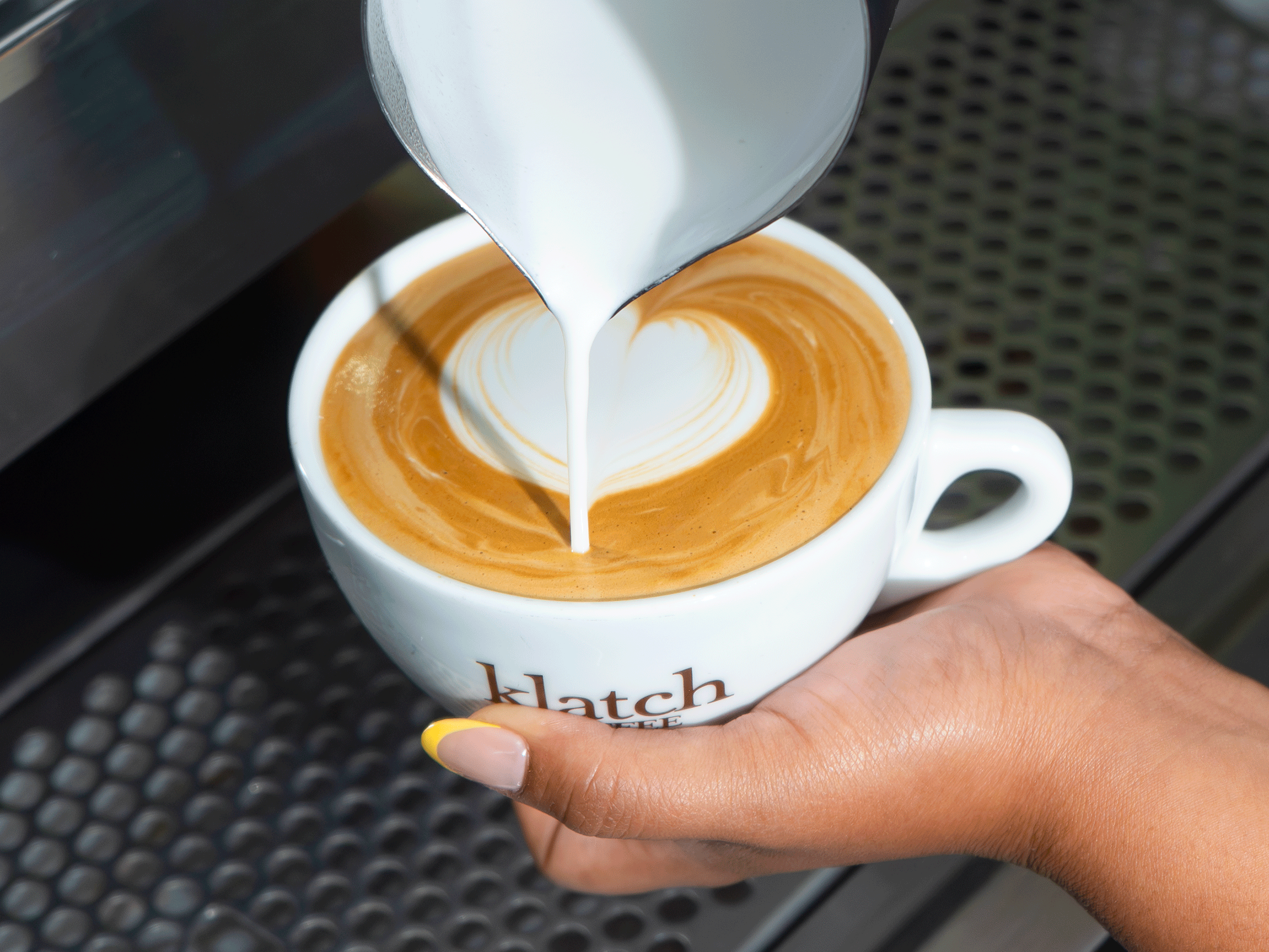 Hands pouring latte art into a mug.