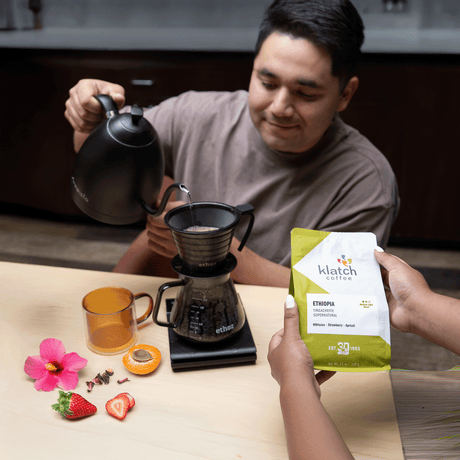Man pouring hot water brewing pour over of with woman's hands holding bag of Ethiopia Supernatural.