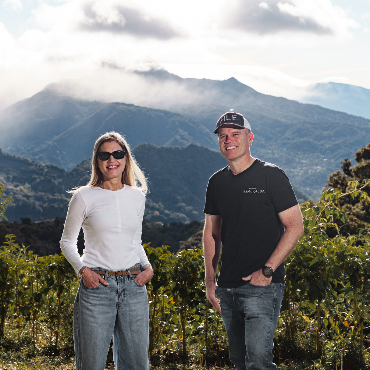Rachel Peterson and brother Daniel Peterson standing in a scenic outdoor setting with coffee trees and mountains in the background.