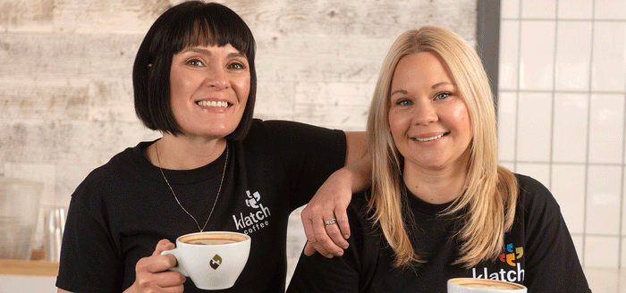 Two girls smiling at the camera while holding latte mugs.