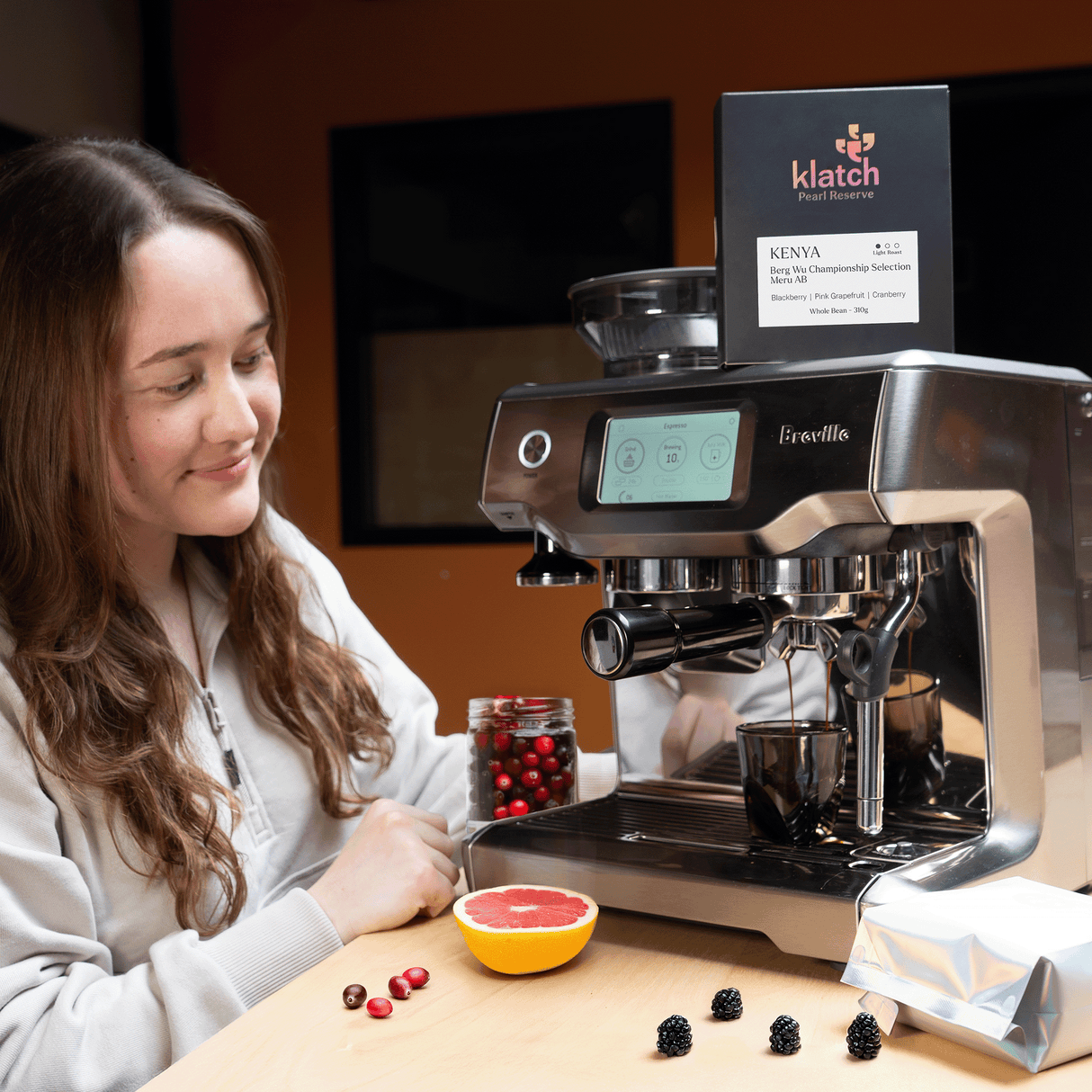 Woman using a Breville espresso machine with klatch coffee packaging in the background.