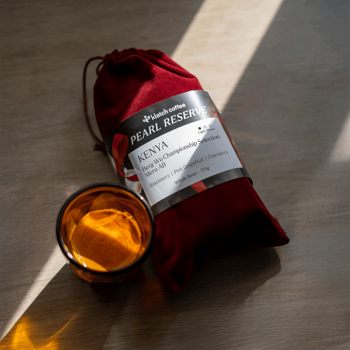 Red velvet bag with a Kenya Berg Wu label next to a shot of espresso in an orange cup.