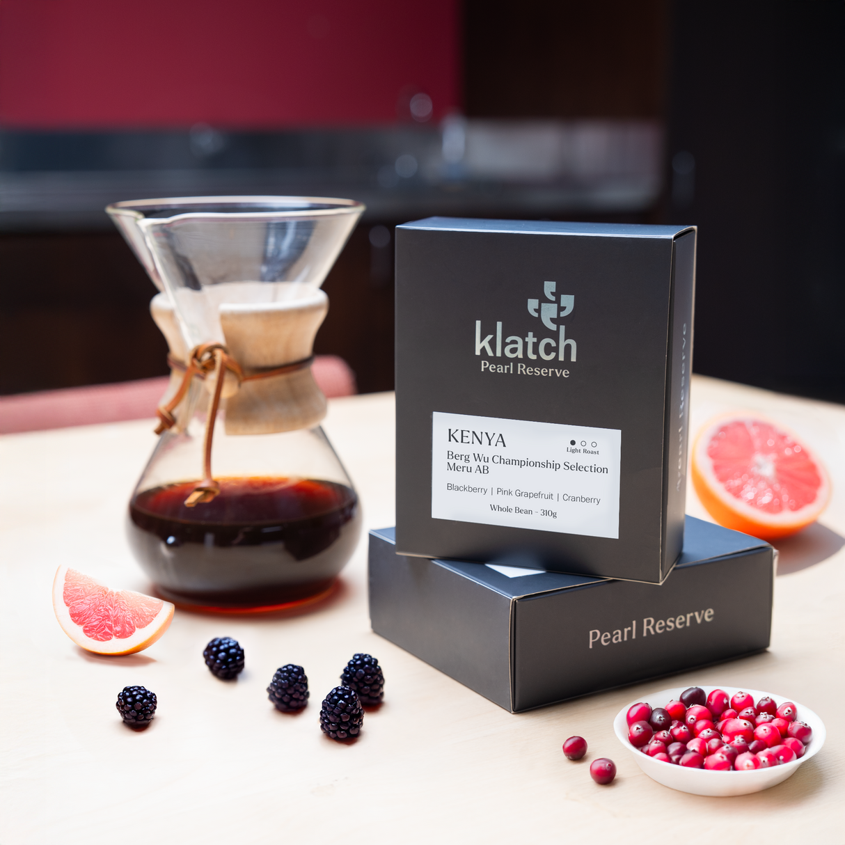 Chemex coffee maker with Klatch coffee Pearl Kenya Berg Wu package on a table with fruits and berries.