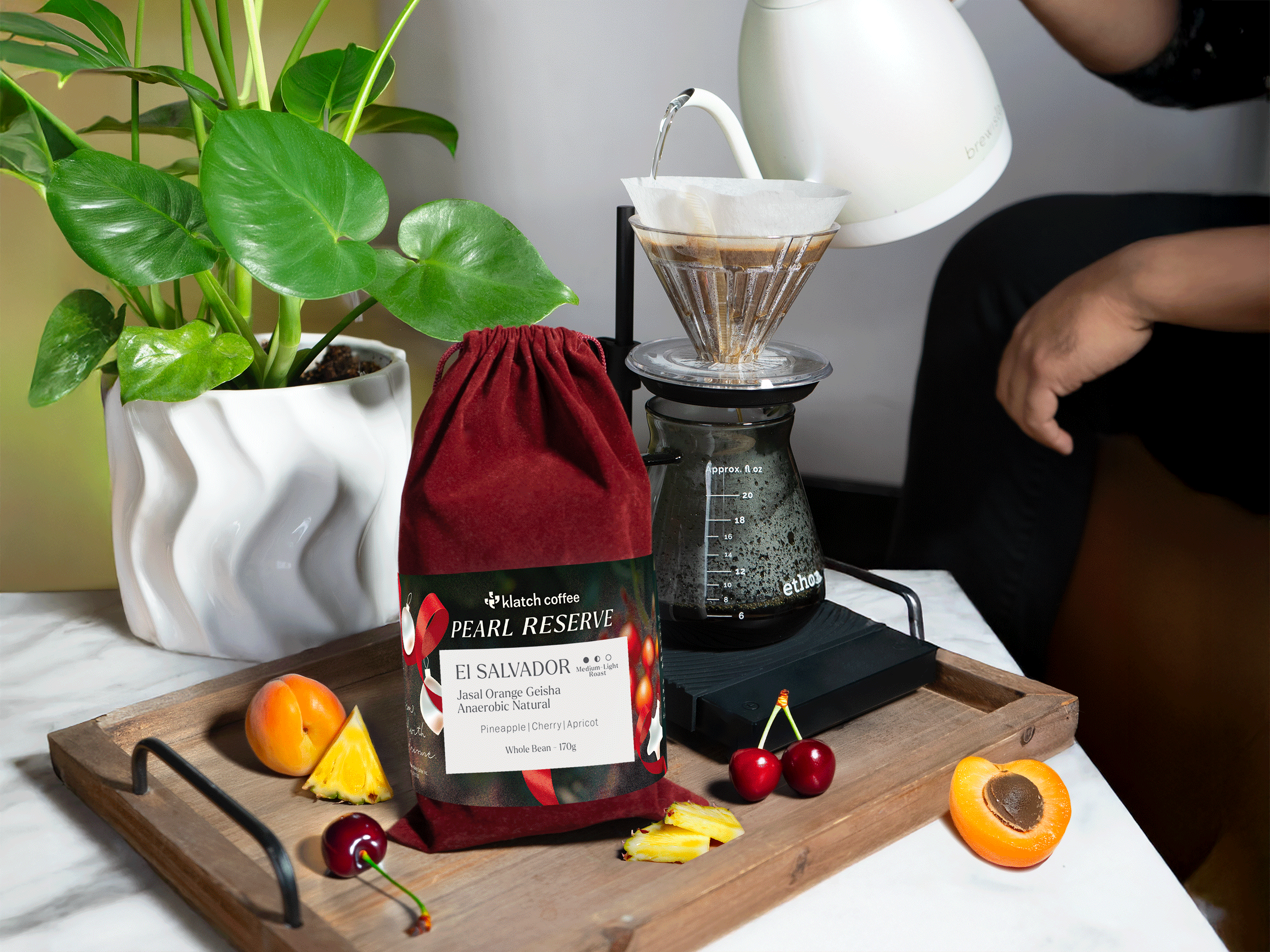 Pearl Reserve coffee in a velvet bag on a table, surrounded by cherries, apricot, and pineapple.