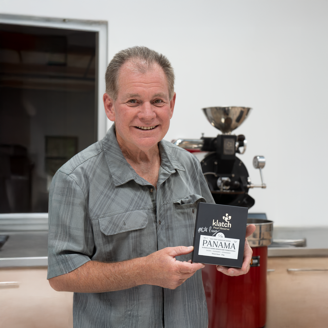 Mike Perry smiling at camera while holding Klatch Panama Pearl reserve coffee that is signed in silver marker.