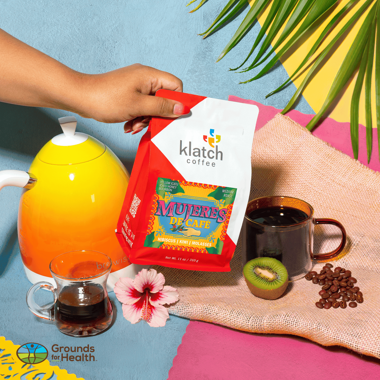 Hand holding a Klatch coffee bag with a colorful background featuring a kettle, coffee cups, and coffee beans.