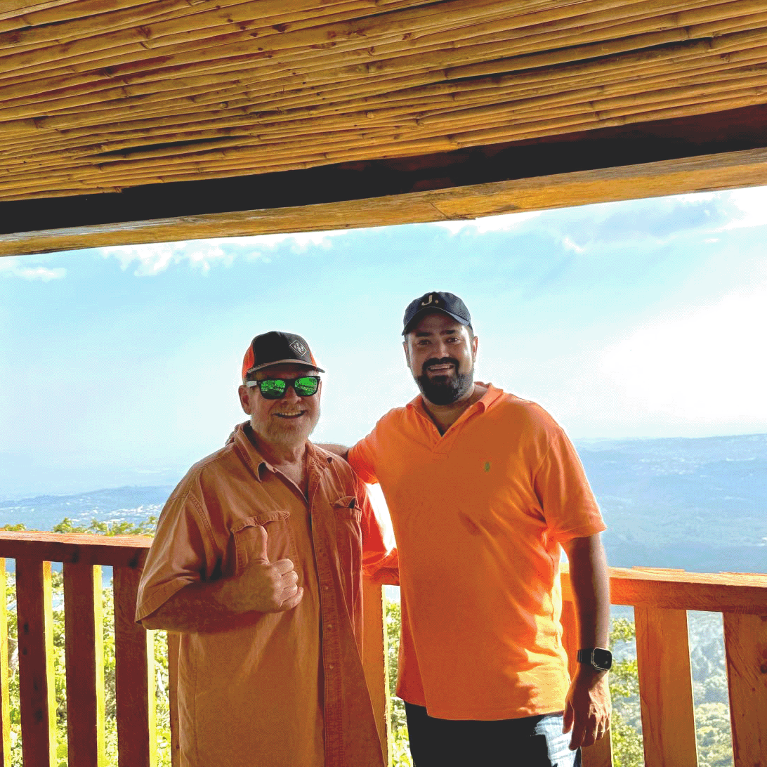Mike Perry and Andres Salaverria standing on a wooden deck with a scenic background in El Salvador.