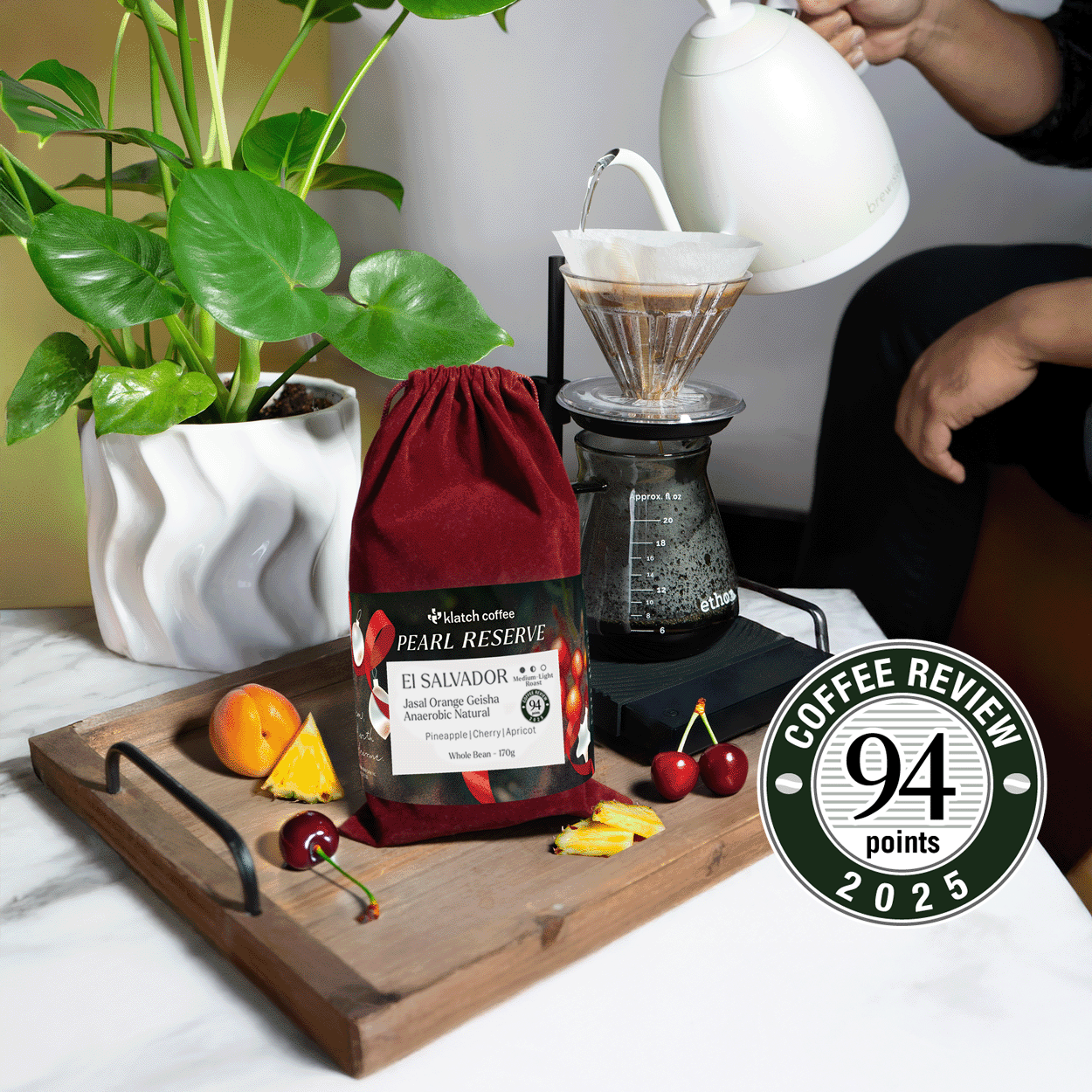 El Salvador Jasal Orange Red Velvet coffee bag on a tray surrounded by pineapple, cherries, and apricots.