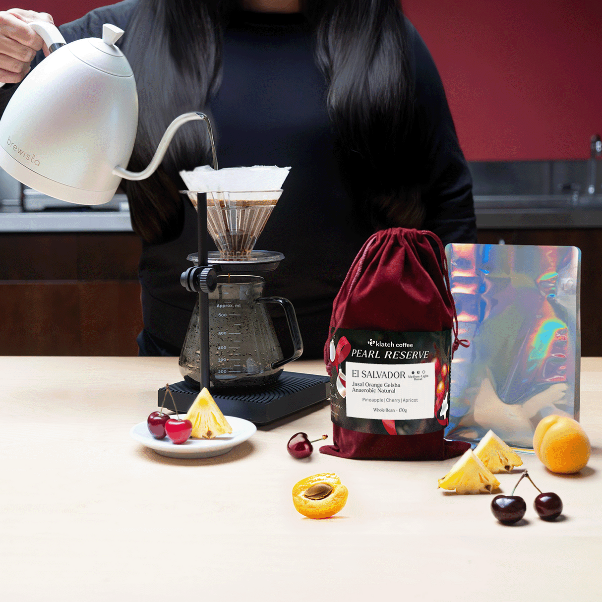 Person pouring coffee using a pour-over setup with a bag of Pearl Reserve coffee on a table.