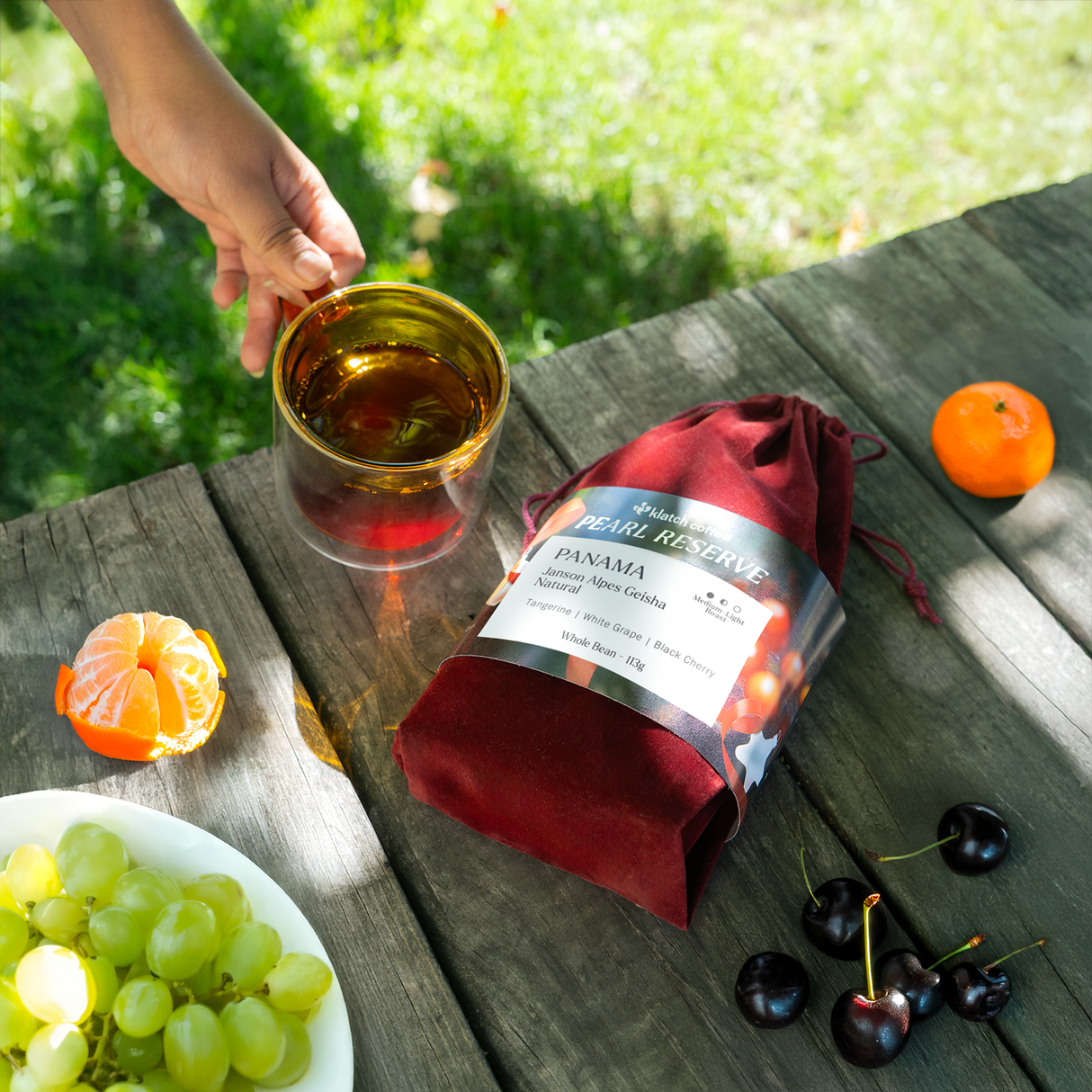 Panama Janson Alpes Geisha Natural red velvet bag on a wooden table with fruits and a cup of geisha.