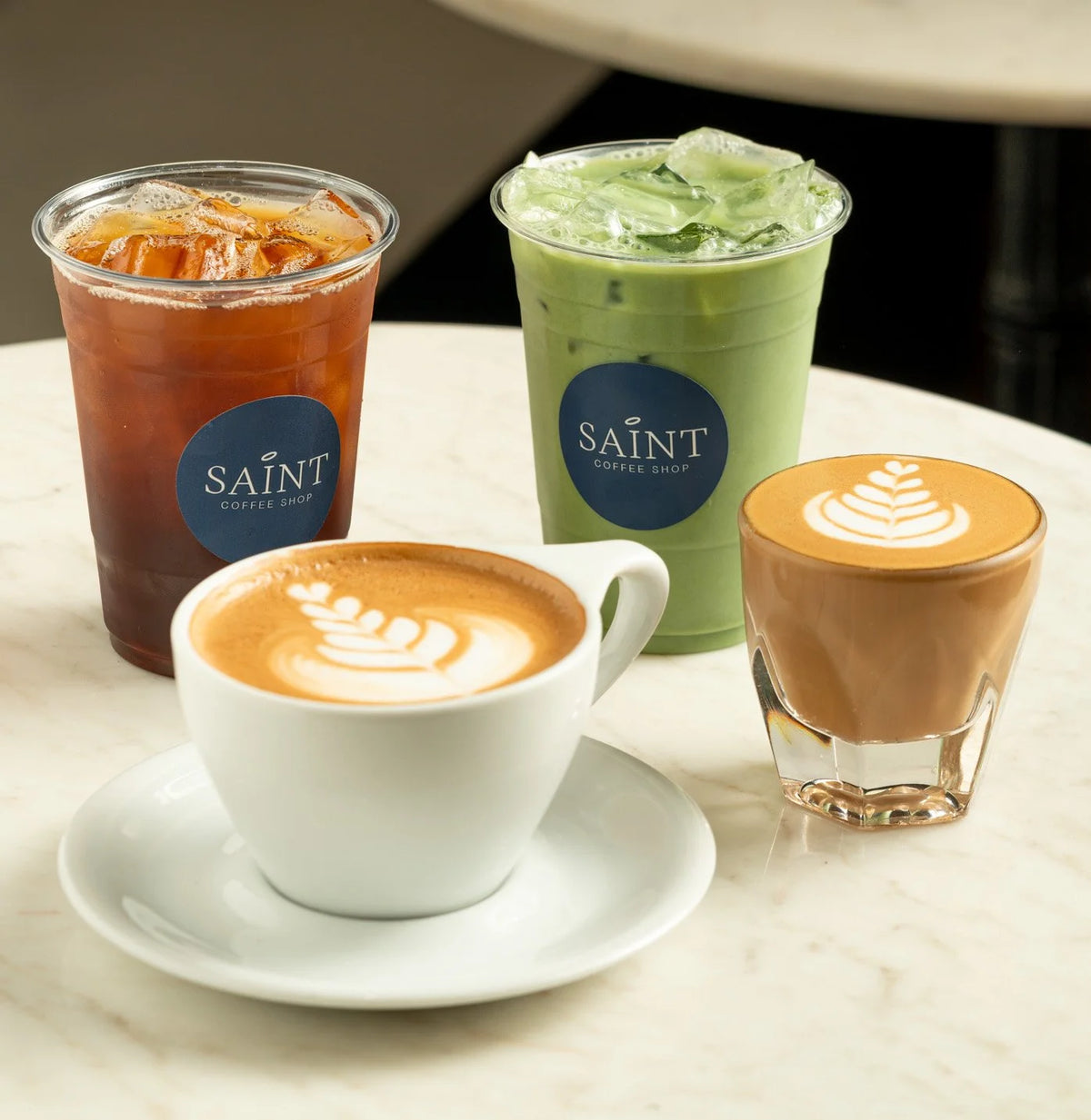 Assortment of coffee shop drinks on a table, including iced coffee, iced matcha, and two lattes with latte art.