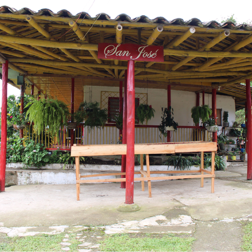 Outdoor setting with a wooden raised African drying bed under a a covered patio, 'San José', surrounded by plants.
