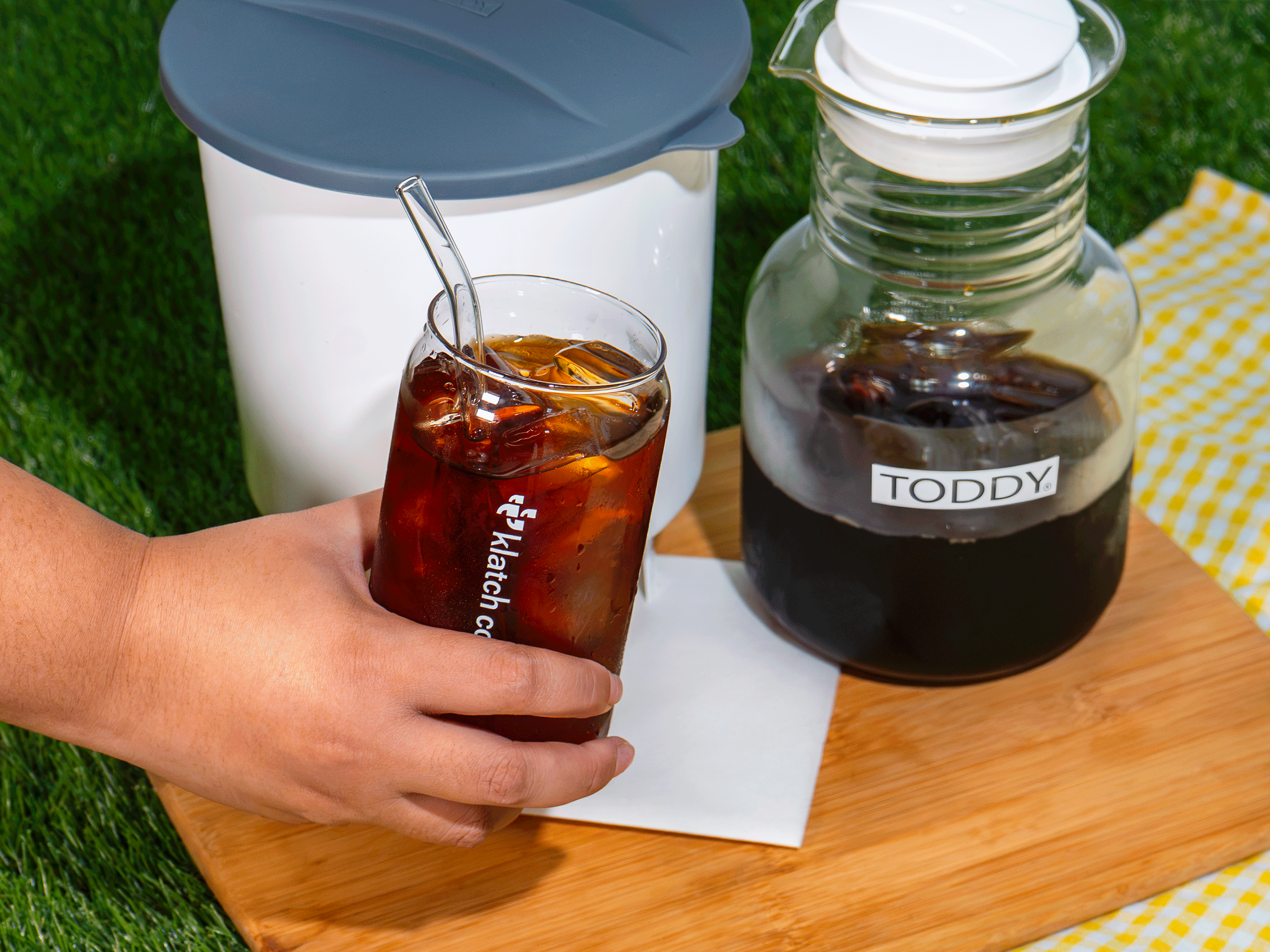 Hand picking up a glass of cold brew in front of a Toddy brewer.