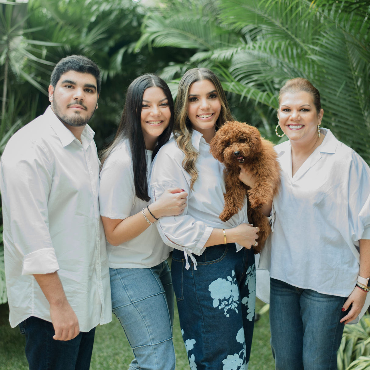 Altieri Family from left to right, Tom, Ale, Chombi holding red-brown dog in arms, Anna Marissa in front of large palm tree leaves..
