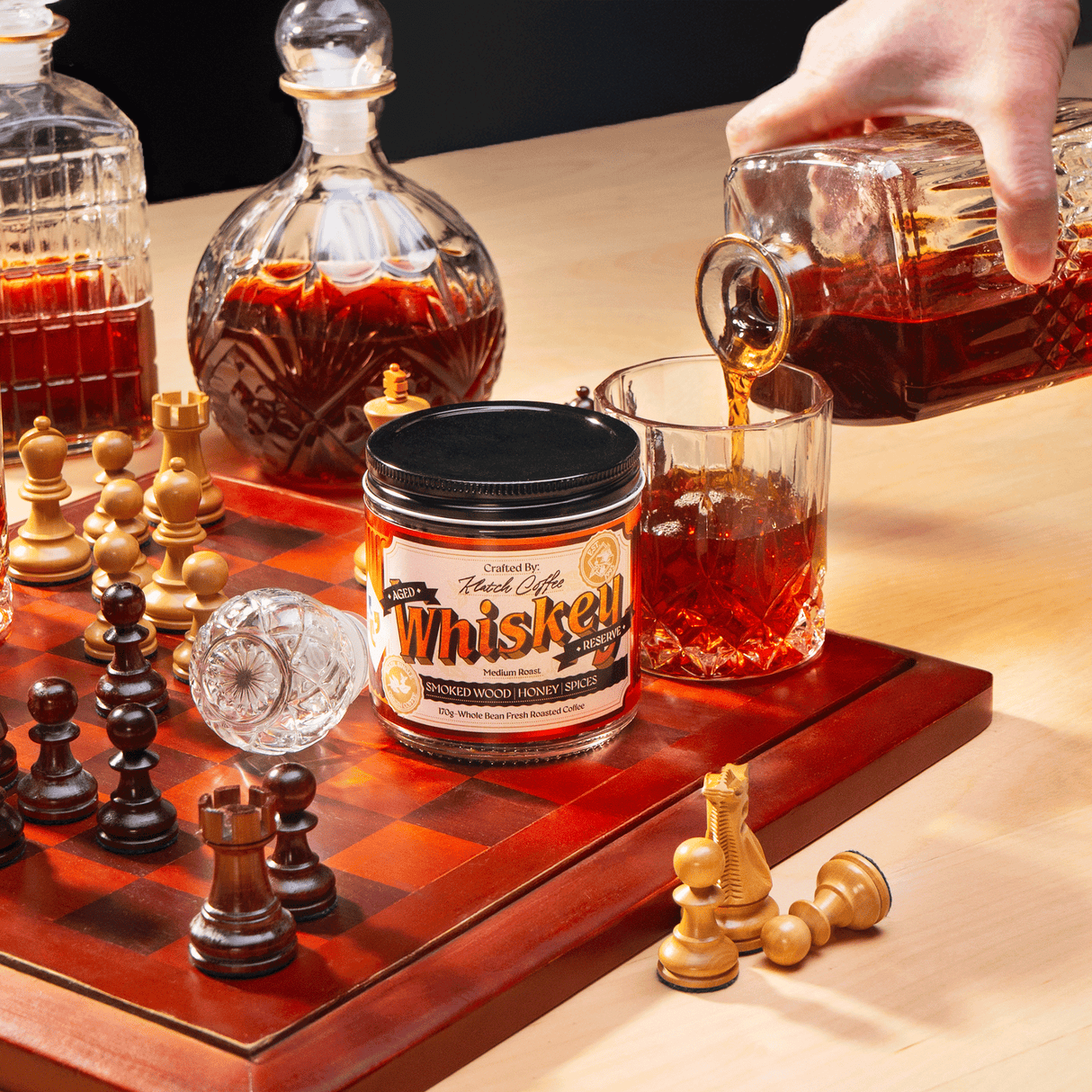 A bottle of Klatch Coffee Whisky Reserve sits on a chessboard while someone pours whiskey into a glass nearby.