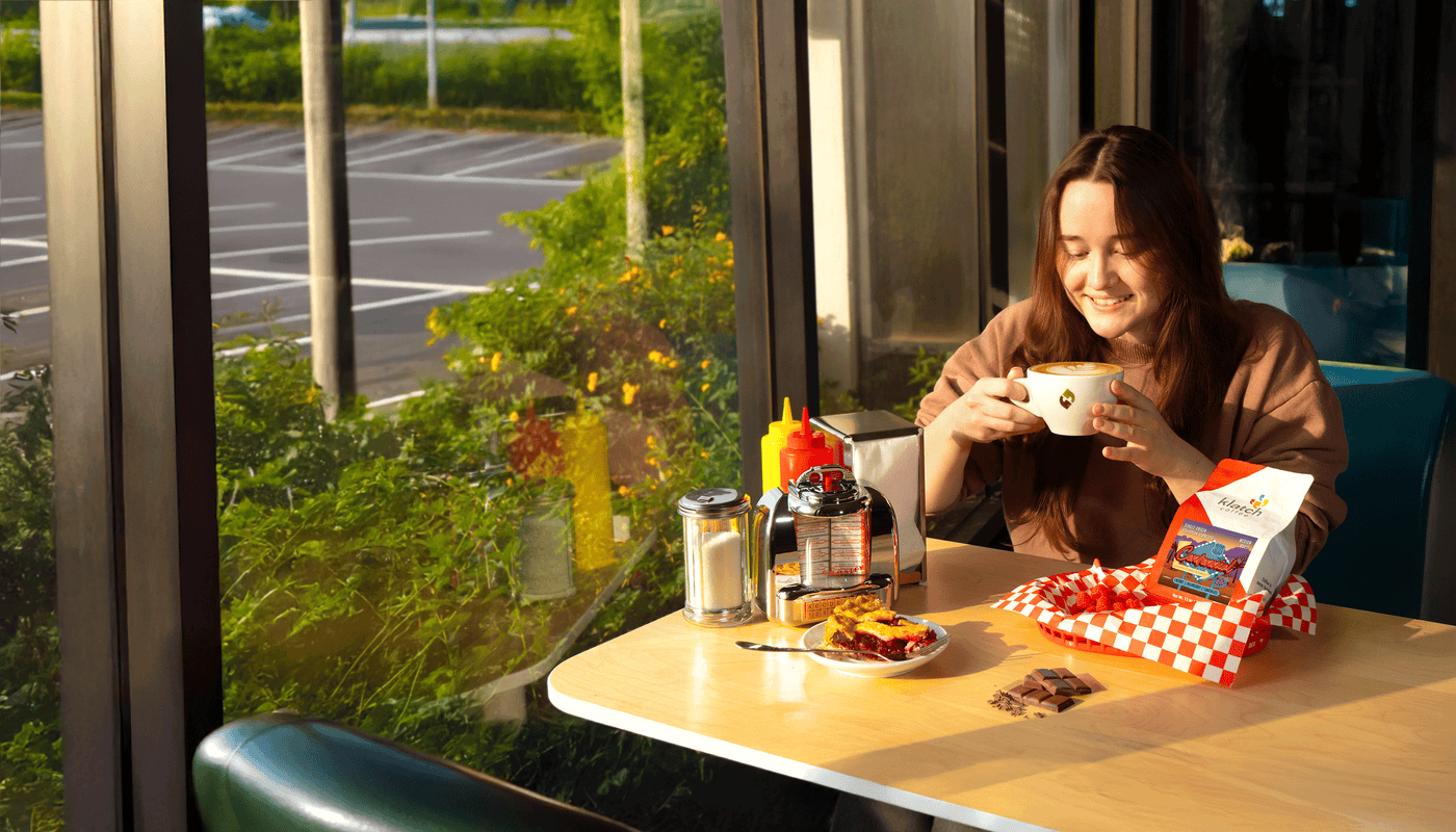 Woman enjoying a latte at a table with a a slice of cherry pie, and a bag of Centennial Espresso.