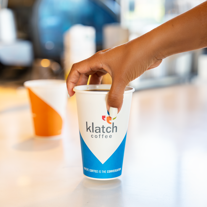 Hand grabbing a 16oz Klatch coffee cup.