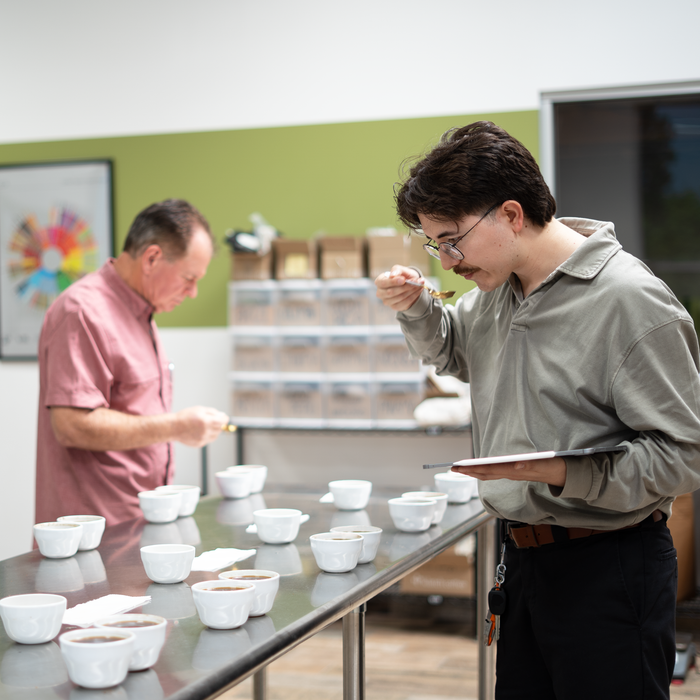 Two men examining ceramic bowls on a table in a room with shelves in the background.
