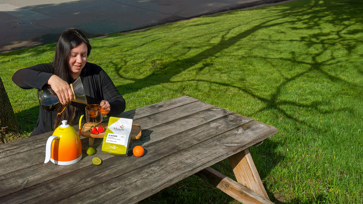 Woman sitting at a wooden picnic table outdoors with a juice box and snacks.