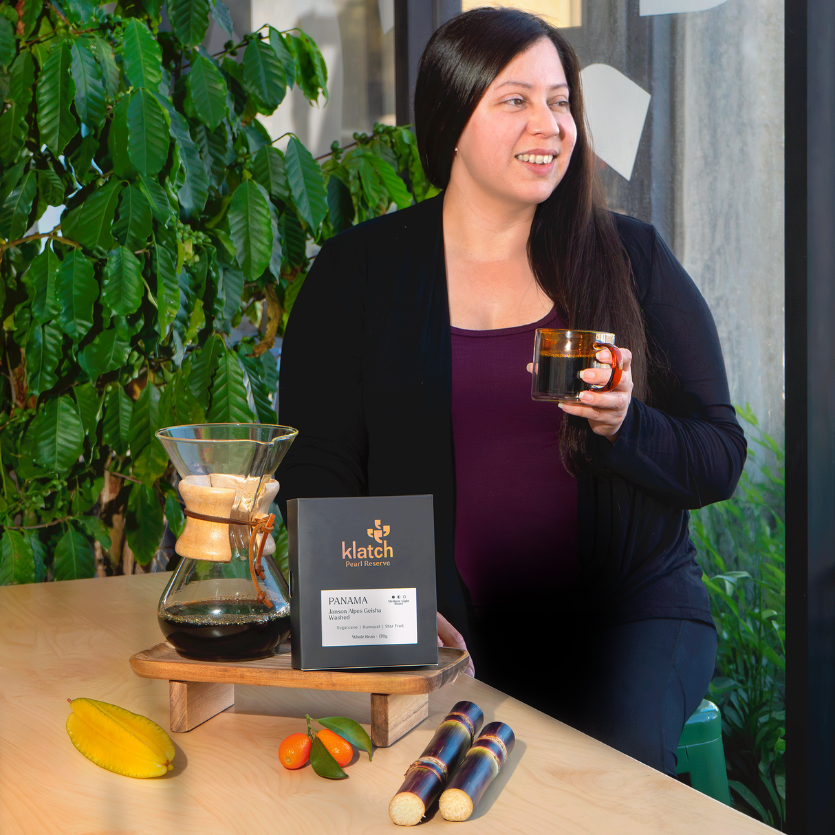 Woman holding a mug with a coffee setup including a Chemex and a Pearl Reserve Coffee on the table.