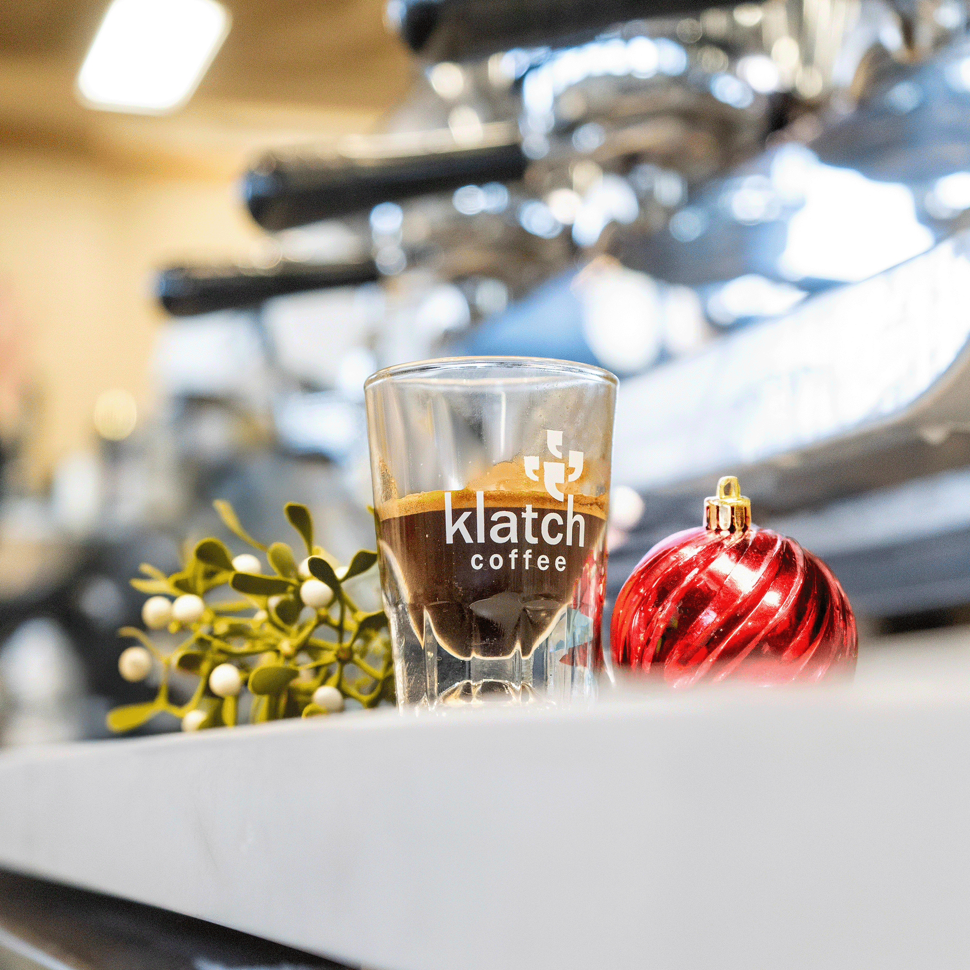Espresso shot with mistletoe and a red ornament beside it.