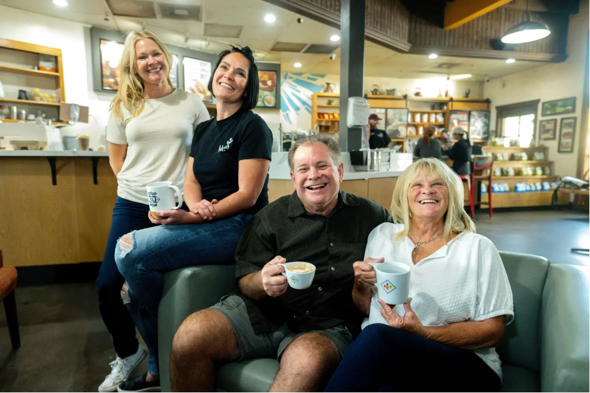 Four people sitting together in a casual setting, holding cups.
