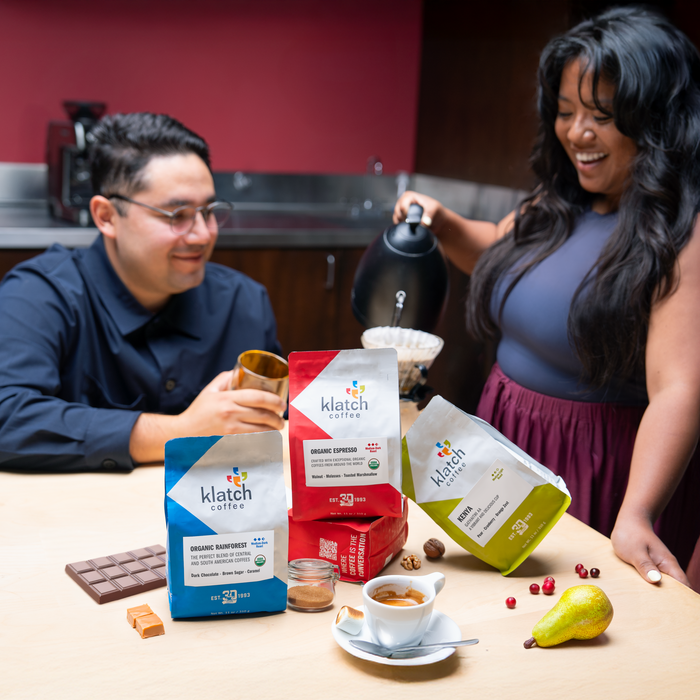 Two people in a kitchen setting with klatch coffee packages and a cup of coffee on a table.