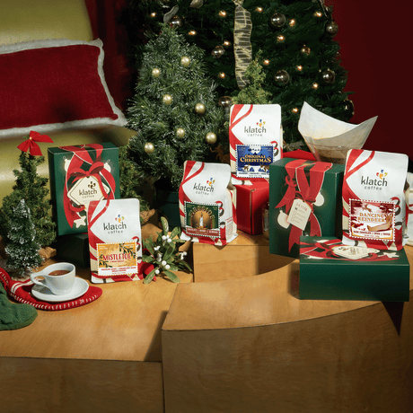 Holiday collection of coffee bags and holiday trios on table with christmas tree in background.