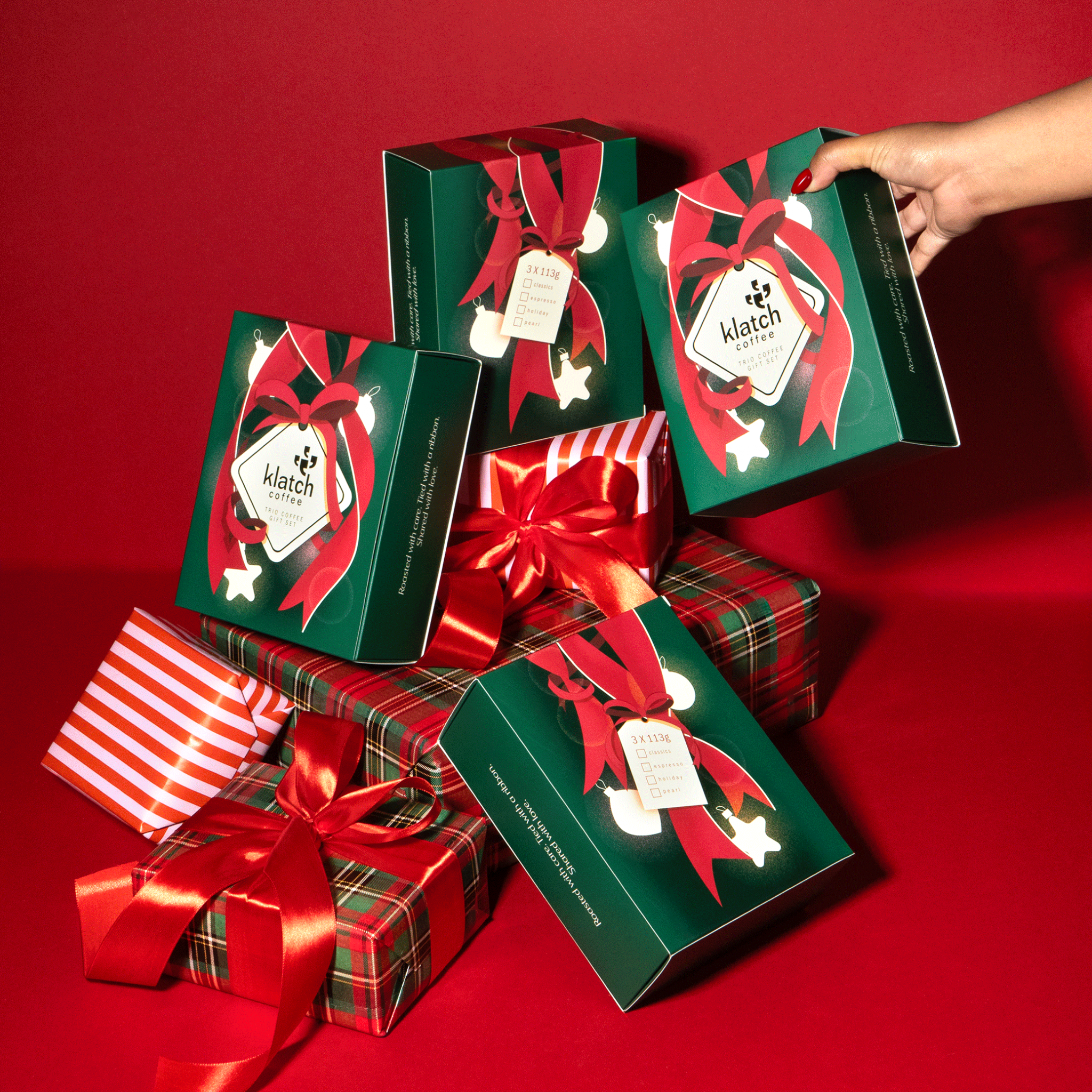 Stack of Trio Gift Sets and gift boxes with red ribbons on a red background
