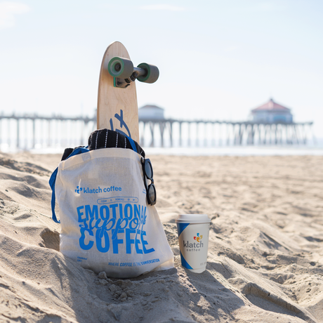 Skateboard with a bag and cup on a sandy beach with a Huntington Pier in the background