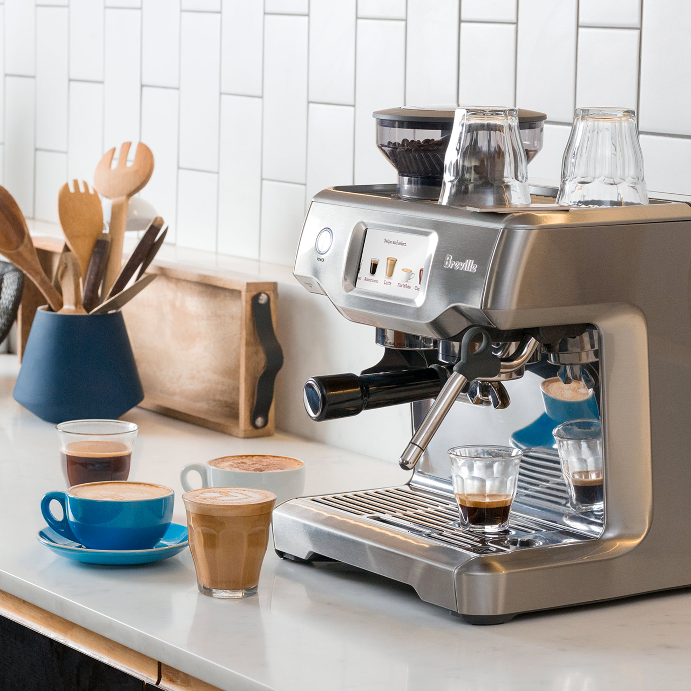 Breville espresso machine on a kitchen counter surrounded by freshly prepared espresso, lattes, and cappuccinos.