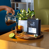 Altieri Alessa Washed Pearl Box with glass cup of coffee, potted plant on round tray sitting on wooden table.  And person pouring black coffee with lemon zest, jasmine and bergamot.