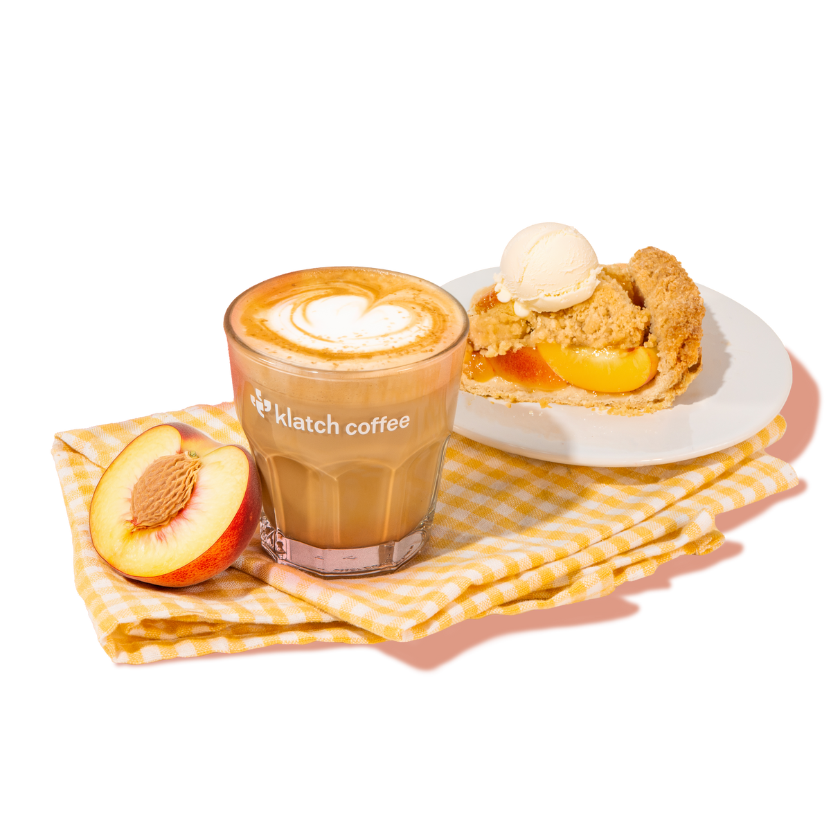 Klatch Coffee latte with heart-shaped latte art beside a slice of peach pie topped with vanilla ice cream and a fresh peach half.