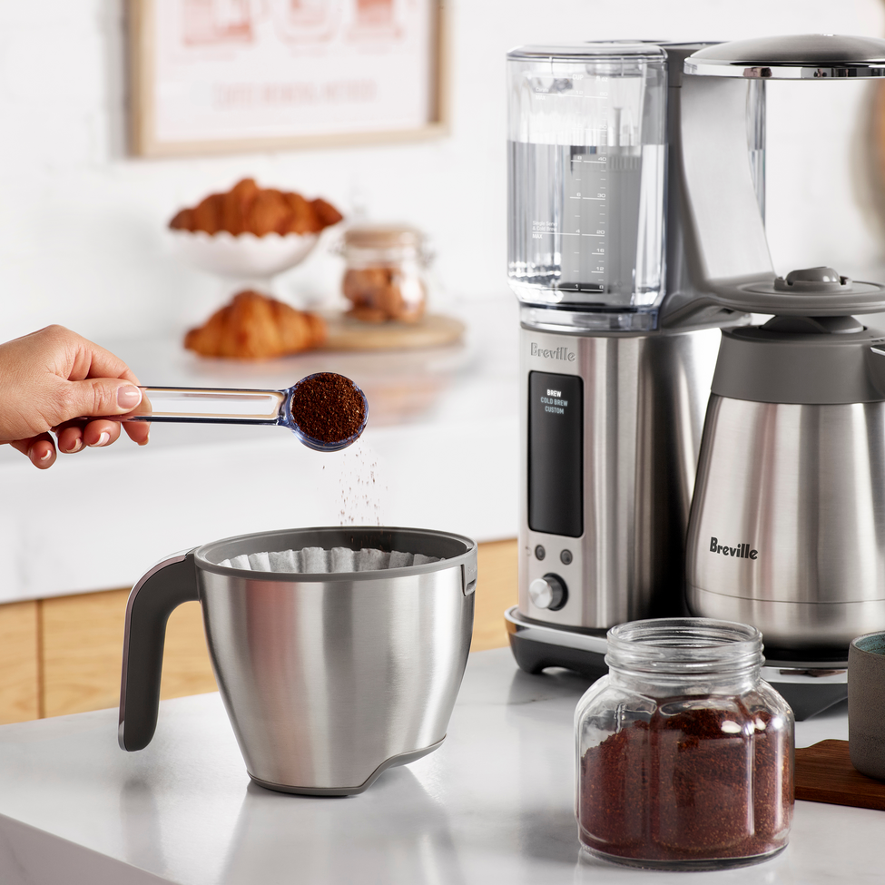 Breville coffee maker on a kitchen counter with a person measuring coffee grounds.