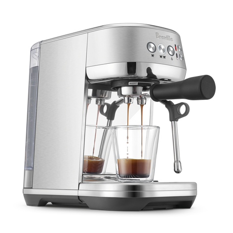 Breville Bambino Plus Espresso Machine with a glass cup of espresso coming out of portafilter on a white background