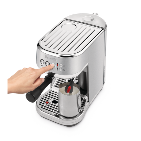 Breville Bambino Plus Espresso Machine with a hand pressing a button on a white background
