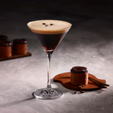 Espresso mocktail in a martini glass with a chocolate cake and coffee beans on a dark background