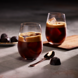 Two glasses of iced espresso drinks on a dark surface with chocolate truffles.