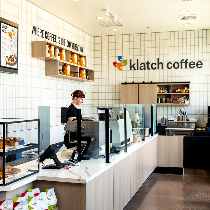 Barista working behind a counter at Klatch coffee, preparing drinks.