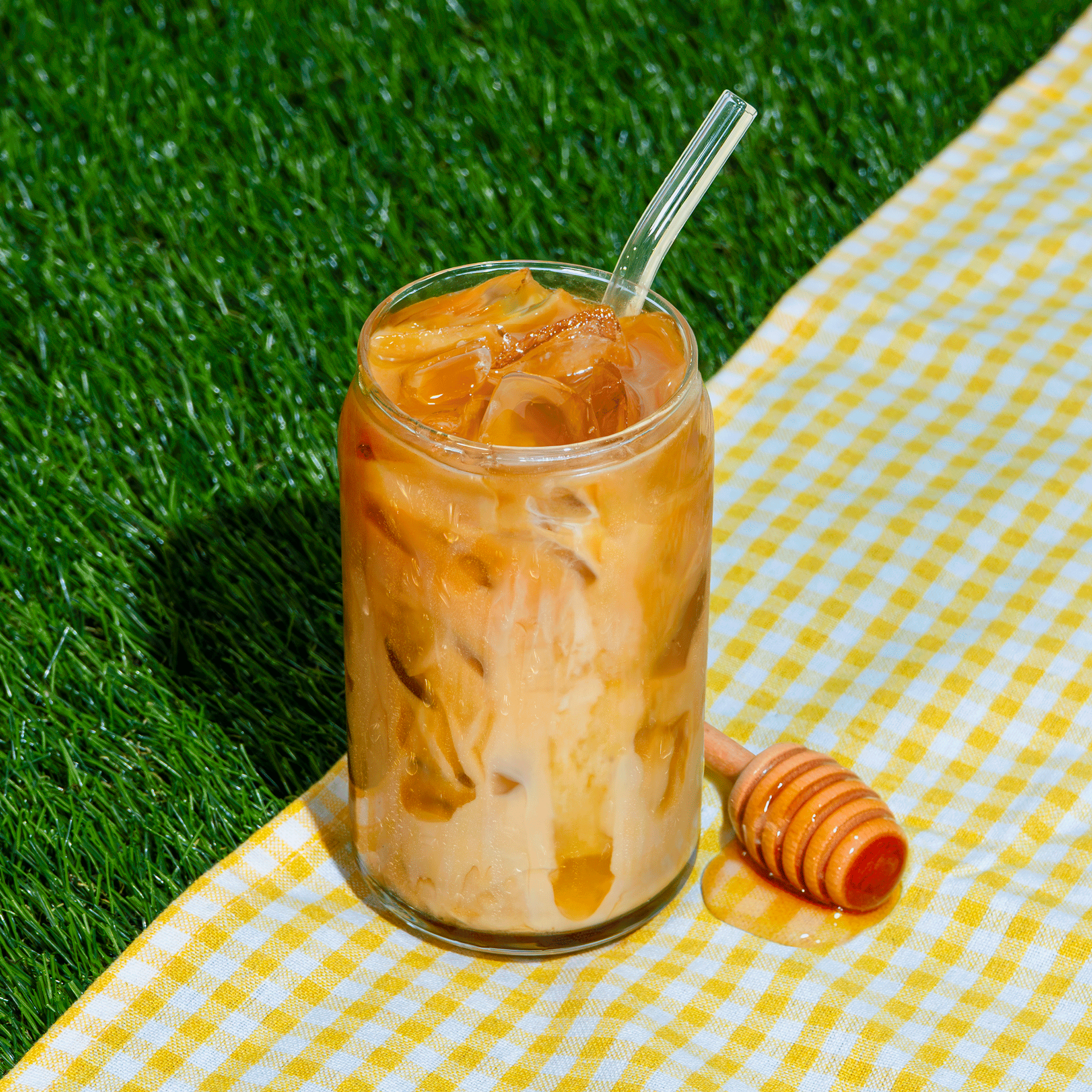 Glass of Klatch Coffee's Bee's Knees Lime drink on a grassy background beside a honey stick.