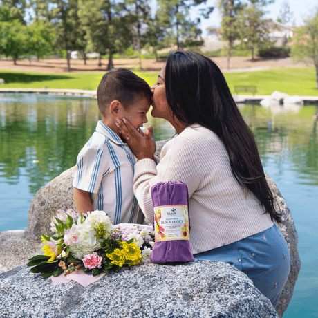 Mother kissing her son’s head at a lake, with Klatch Coffee’s Black Honey Pearl Reserve Coffee in the foreground beside flowers.