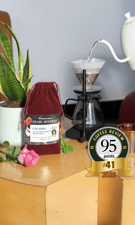 Coffee bag labeled 'Pearl Reserve Colombia' with a coffee brewing setup and a coffee review score badge.