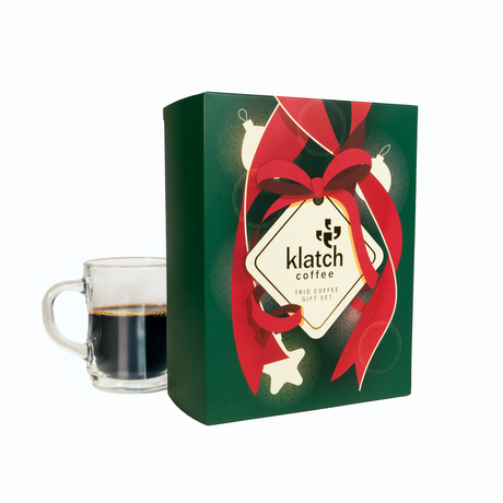 Holiday Gift set box with red ribbon and 'Klatch Coffee' branding next to a glass of coffee.