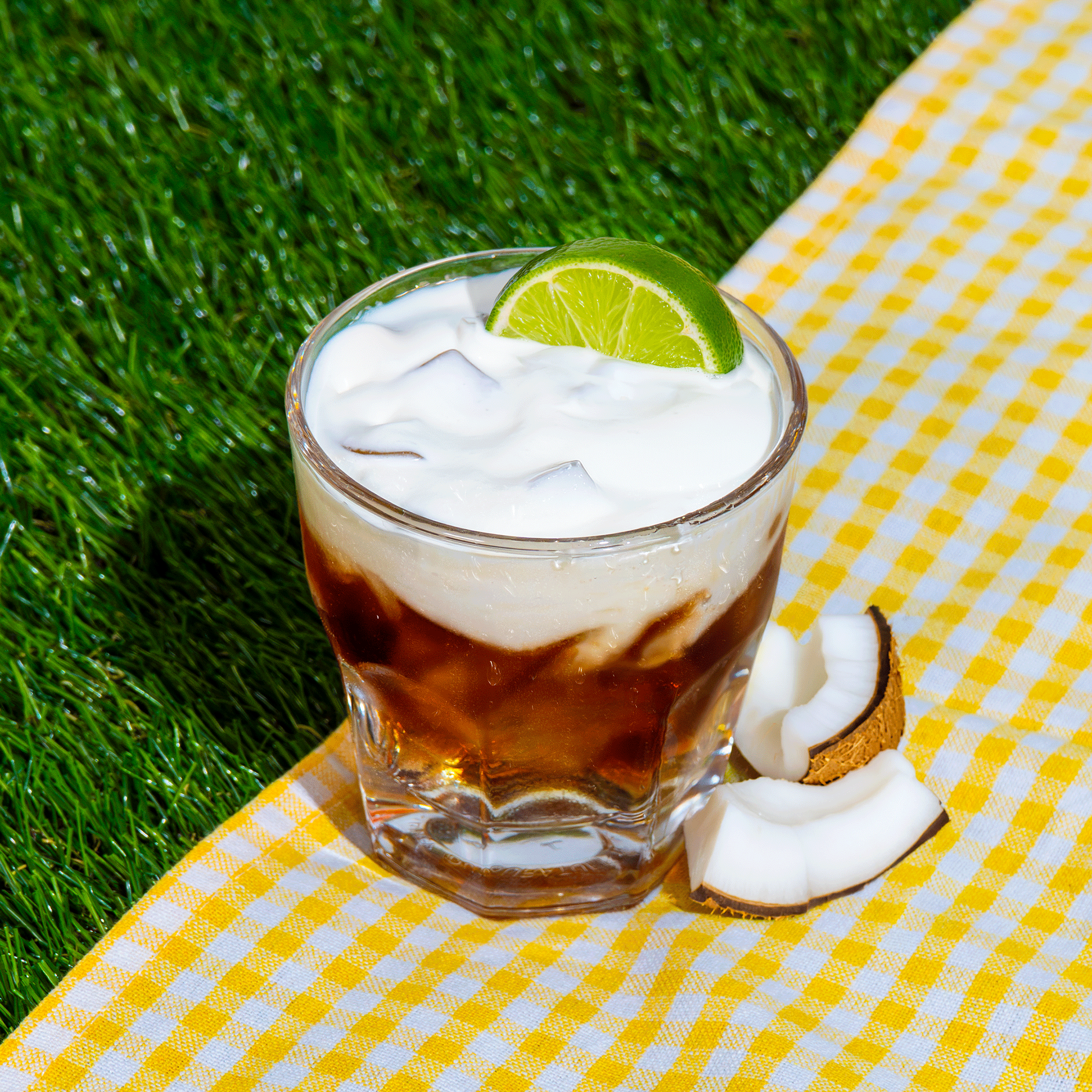 Glass of Klatch Coffee's Cooling Coconut Lime drink on a grassy background beside pieces of coconut.